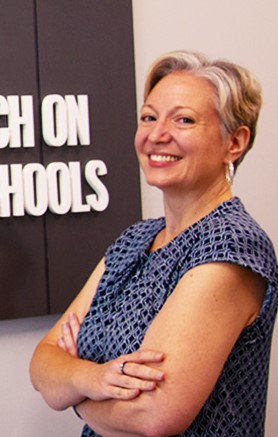 Smiling white woman with short side-parted silver hair, wearing a blue cap-sleeve shirt and silver hoop earrings